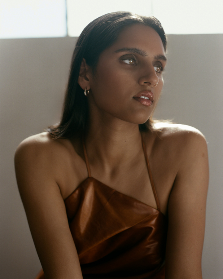 Portriat of a Model looking away from the camera with smokey eye makeup on wearing a copper colored top agianst a neutral background